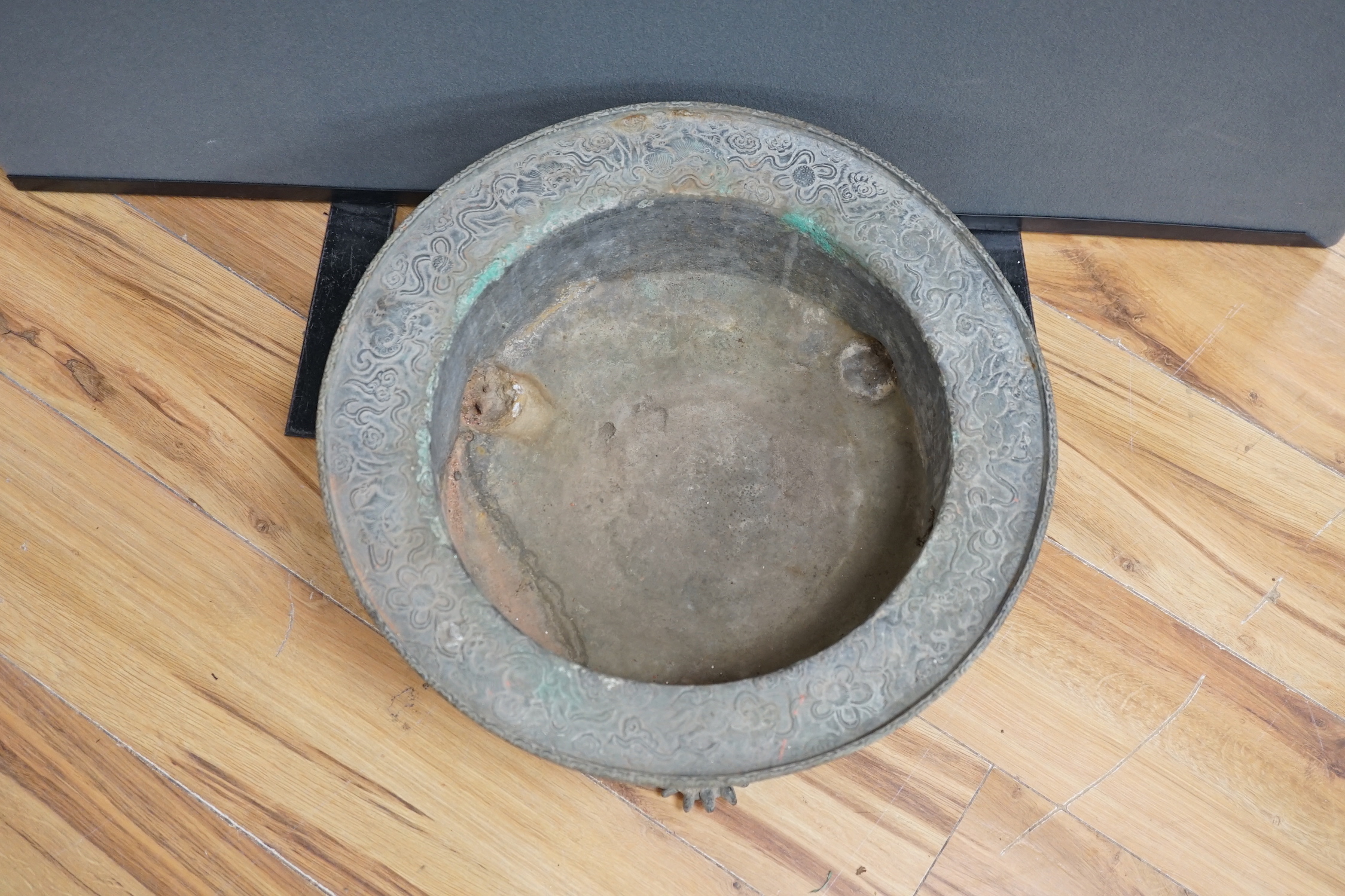 A large and heavy Chinese bronze tripod basin, Xuande mark but 19th century, the broad rim cast in relief with lions, brocaded balls and ribbons, the sides with dragons chasing flaming pearls, on three mythical beast hea